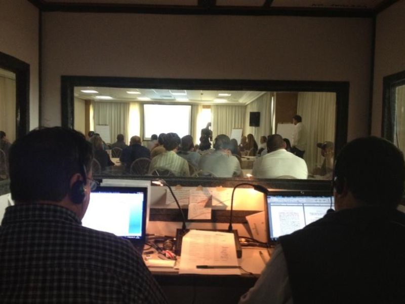 Equipe técnica operando central de tradução simultânea com fones de ouvido e monitores durante evento corporativo, ambiente de sala de controle, fotografia realista